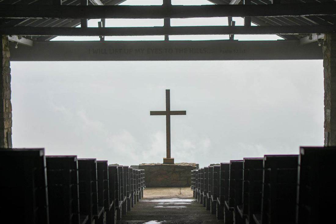 Cruz central e bancos de uma igreja aberta à paisagem