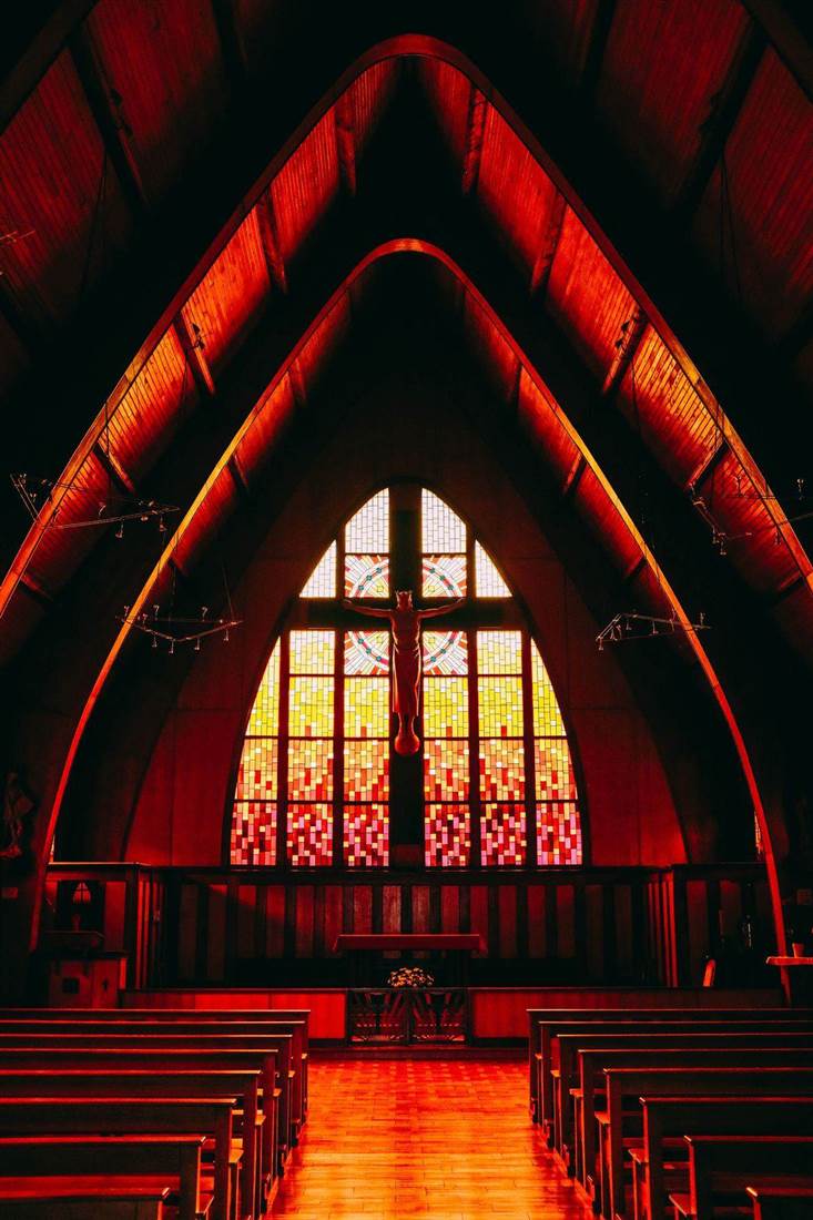 Interior de igreja com bancos de madeira e vitrais iluminados